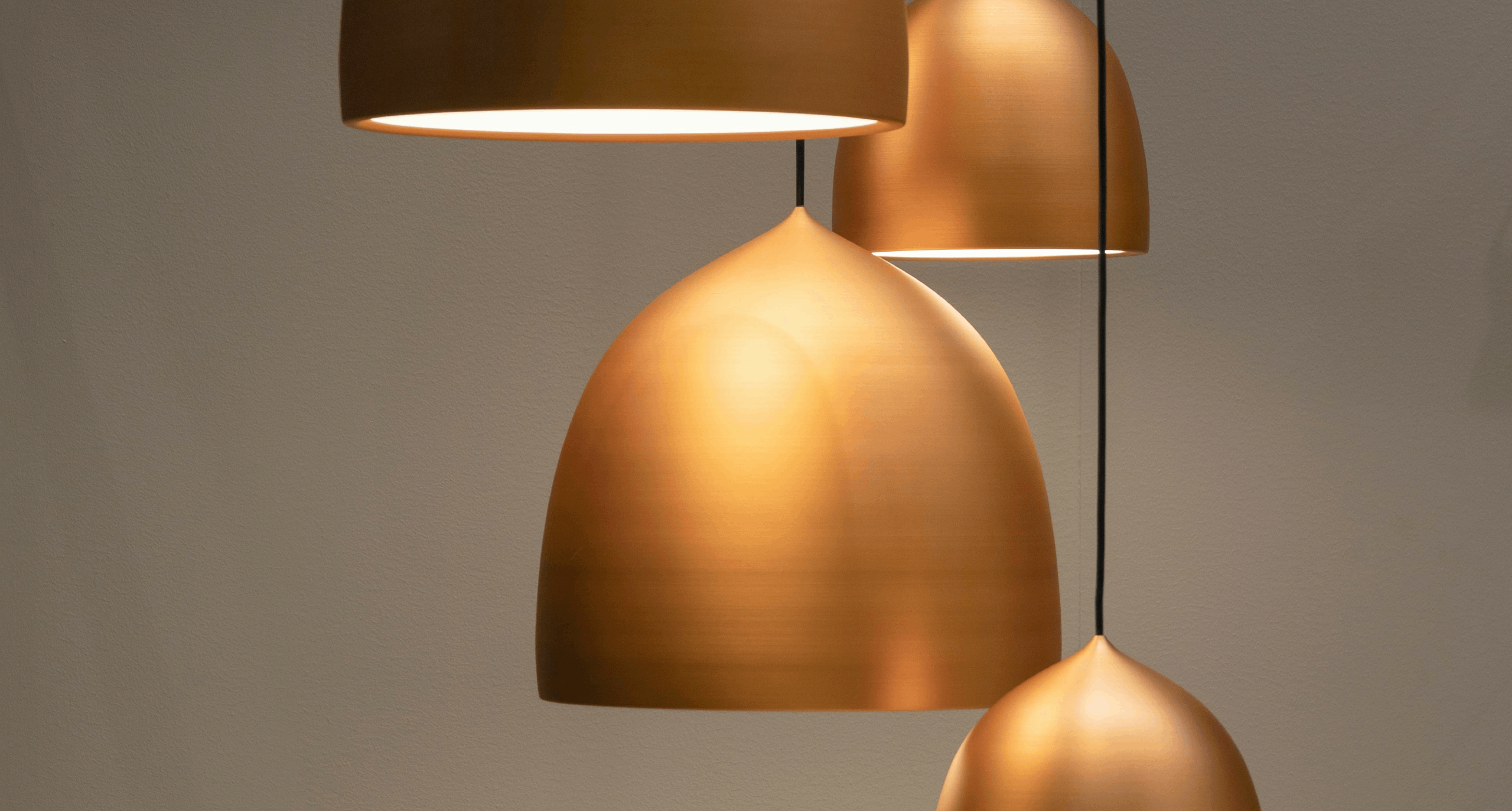 Modern gold pendant lights hanging from the ceiling, casting a warm glow, with three different shapes and sizes against a neutral background.